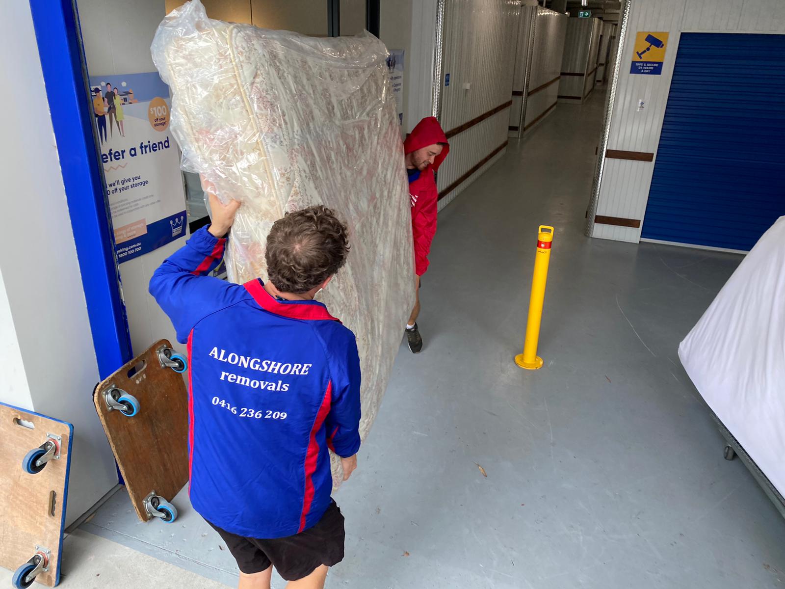 Alongshore crew moving a wrapped mattress into a secure storage unit